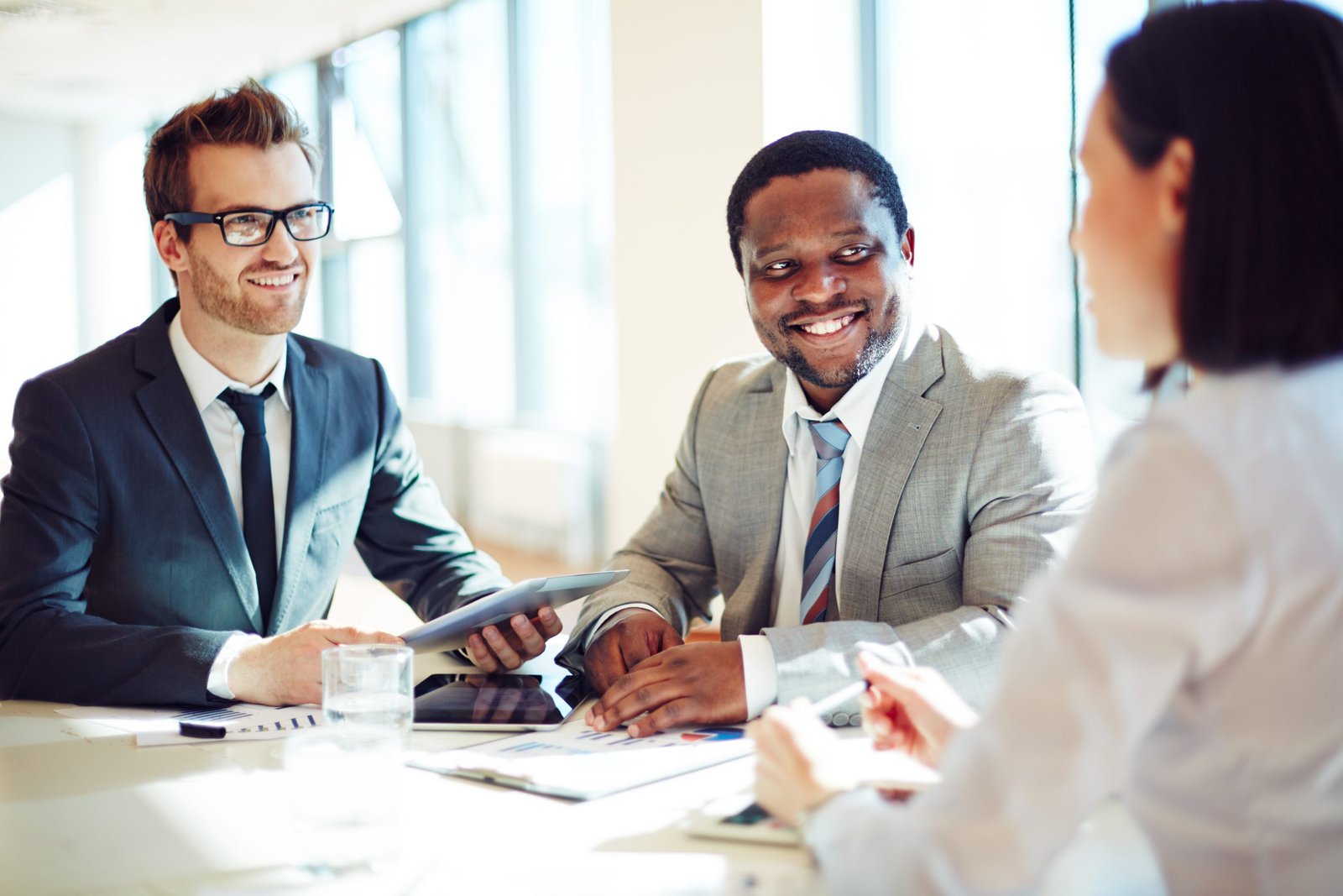three people smiling and having a business conversation with computer tablets in front of them