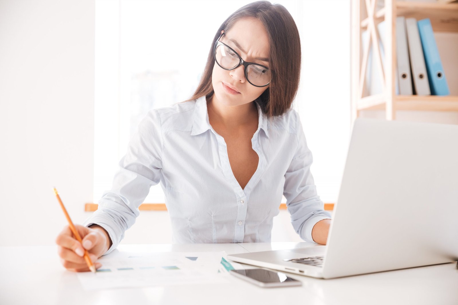 Closeup image of mans hand writing in notebook woman sat at a desk in front of her laptop, concentrating on writing notes